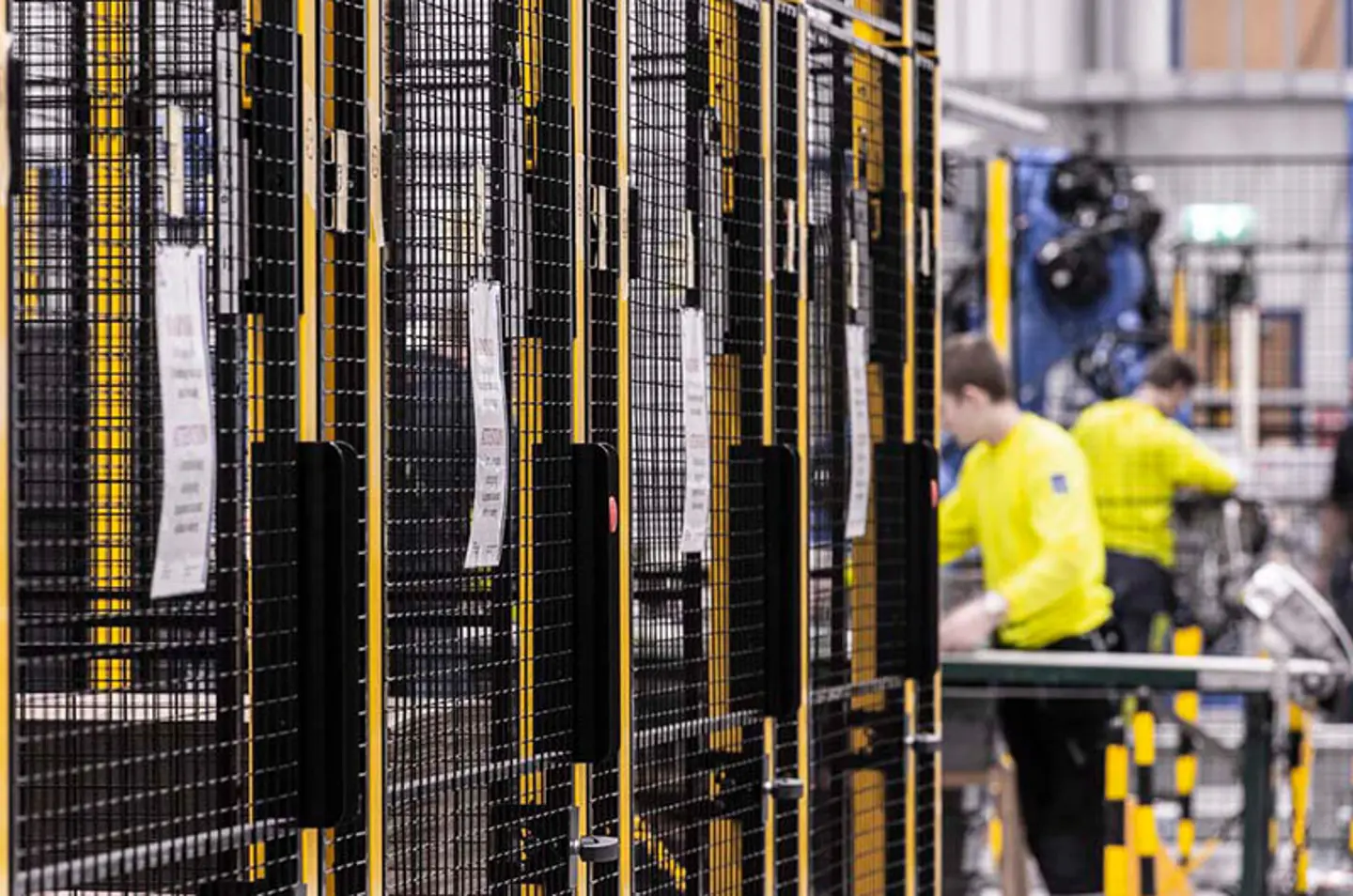 Arbejdere på en fabrik, ved siden af sorte og gule sikkerhedsbarrierer med metalnetpaneler