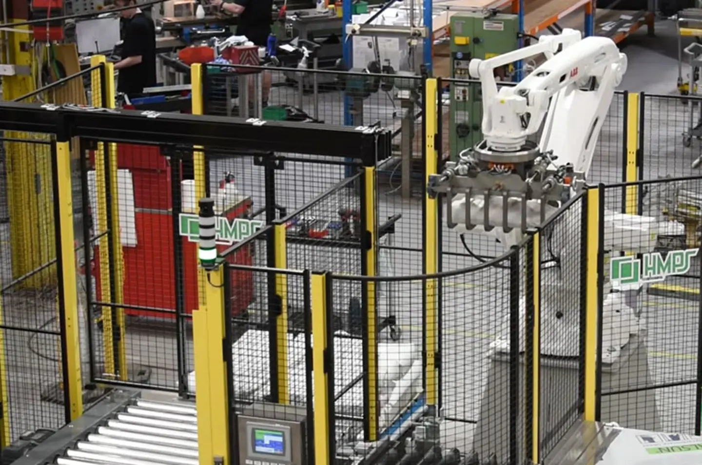 Automatiseret industriel robotarm, der arbejder i en fabrik med transportbånd og sikkerhedsafskærmning